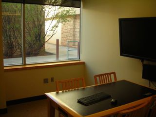 image of study room showing table, 4 chairs wall mounted computer with keyboard and mouse on table