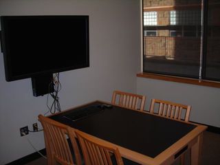image of study room showing table with 4 chairs and wall mounted TV/PC