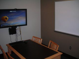 image of study room showing table with 4 chairs, wall mounted TV/PC on left wall and whiteboard on right wall