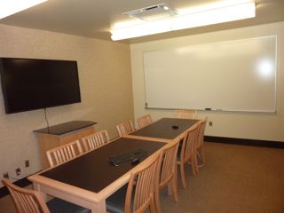 image of study room showing table with 10 chairs, wall mounted TV/PC on left wall and whiteboard on right wall