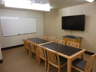 image of study room showing table with 10 chairs, wall mounted TV/PC on right wall and whiteboard on left wall