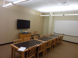 image of study room showing table with 10 chairs, wall mounted TV/PC on left wall and whiteboard on right wall
