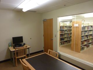 image of study room showing table with 4 chairs, small desk with PC and chair against wall next to door