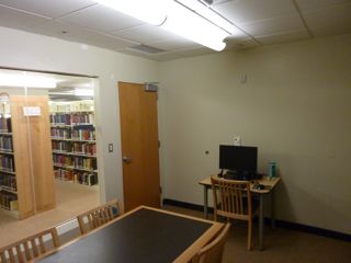image of study room showing table with 4 chairs, small desk with PC and chair against wall next to door