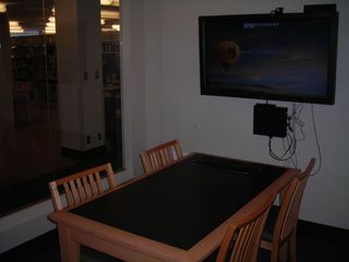 image of study room showing table with 4 chairs and wall mounted TV/PC