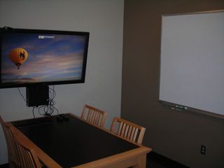 image of study room showing table with 4 chairs and wall mounted TV/PC on left wall and whiteboard on right wall.