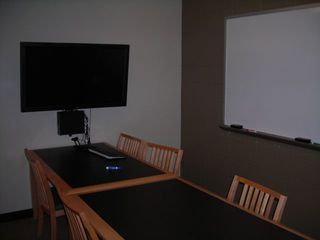 image of study room showing double table with 8 chairs and wall mounted TV/PC on left wall and whiteboard on right wall.