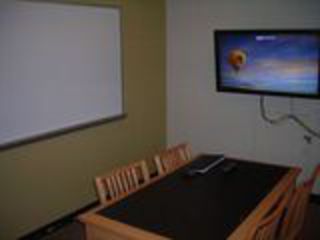 image of study room showing table with 4 chairs and wall mounted TV/PC on right wall and whiteboard on left wall.